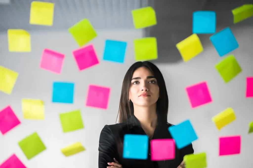 mulher jovem em um ambiente de trabalho cercada por post-its coloridos, representando organização e planejamento estratégico.