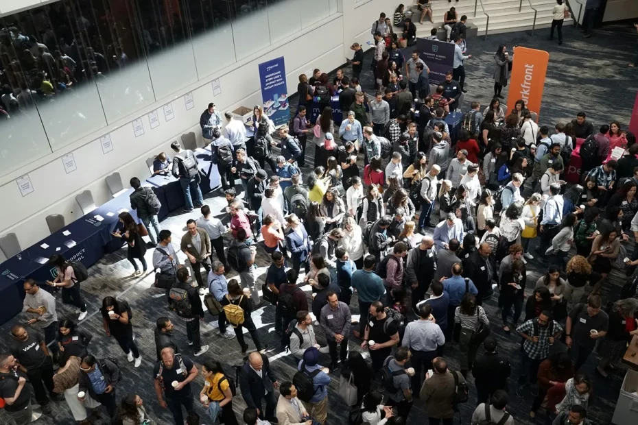 Multidão de pessoas interagindo em um evento de networking com estandes e banners ao fundo.