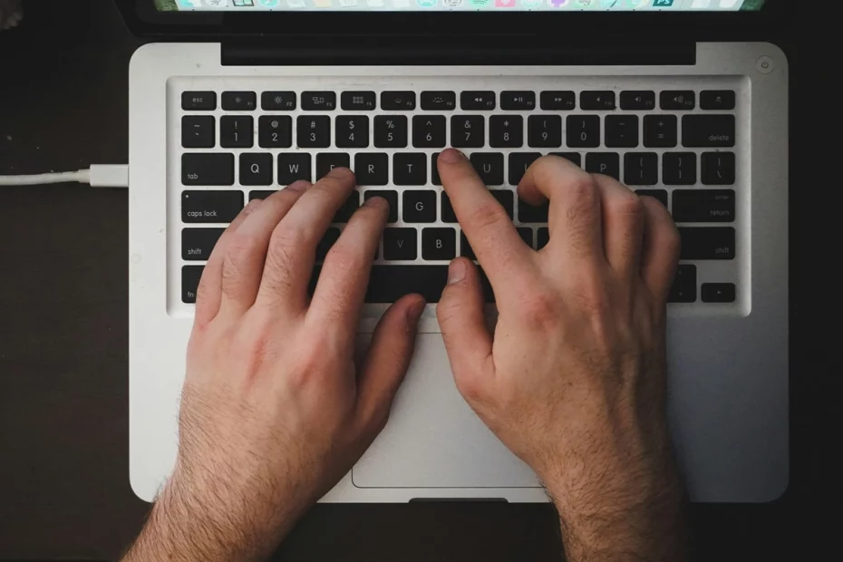 Mãos masculinas digitando em teclado de notebook preto e prata, representando trabalho remoto ou uso de tecnologia.