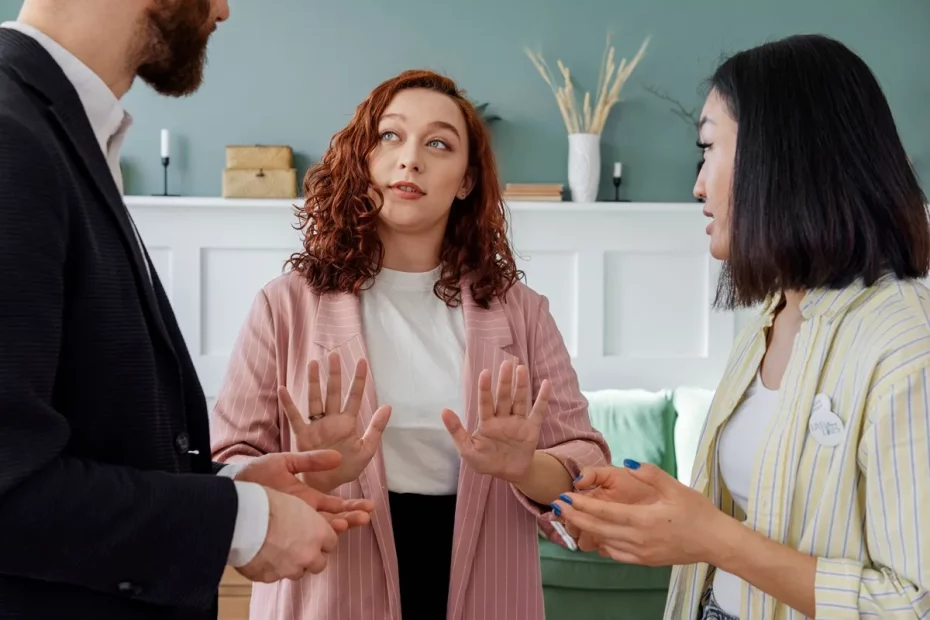 Mulher gesticulando com as mãos enquanto conversa com dois colegas durante uma reunião, demonstrando postura assertiva e expressão séria.