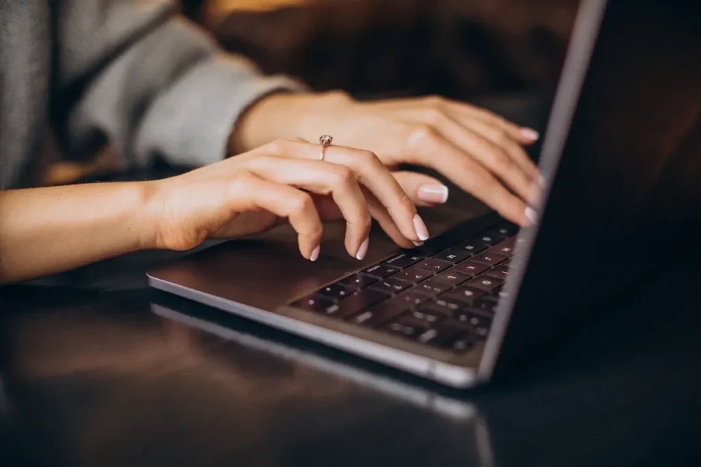 Mãos femininas digitando em um notebook com fundo desfocado e luz ambiente aconchegante