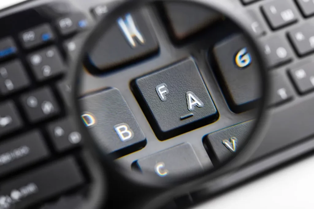 Teclado preto com teclas ampliadas por uma lupa, destacando detalhes das letras.